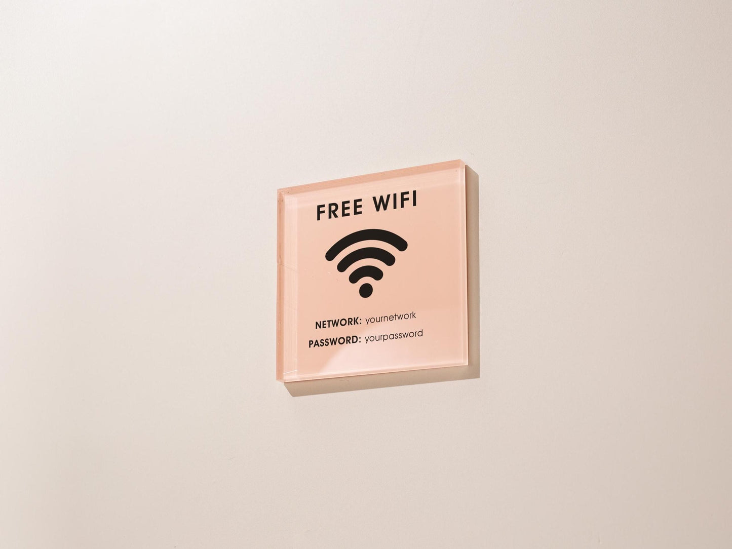 May include: A square, pink acrylic sign with black text and a wifi symbol. The sign reads 'FREE WIFI' at the top, with a wifi symbol in the center. Below the symbol, it lists 'NETWORK: youmetnetwork' and 'PASSWORD: yourpassword'.