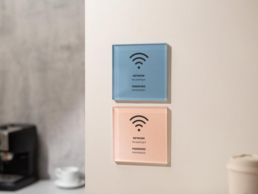 May include: Two square wifi signs mounted on a wall. The top sign is light blue, and the bottom sign is peach. Each sign has a black wifi symbol, the word &#39;NETWORK&#39;, the name &#39;MuuseSigns&#39;, the word &#39;PASSWORD&#39;, and the word &#39;HANDMADE&#39;.