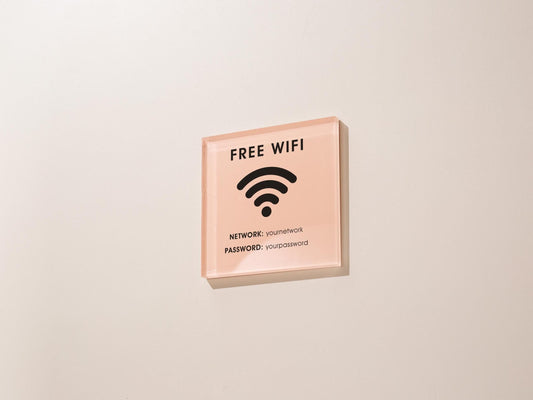 May include: A square, pink acrylic sign with black text and a wifi symbol. The sign reads &#39;FREE WIFI&#39; at the top, with a wifi symbol in the center. Below the symbol, it lists &#39;NETWORK: youmetnetwork&#39; and &#39;PASSWORD: yourpassword&#39;.