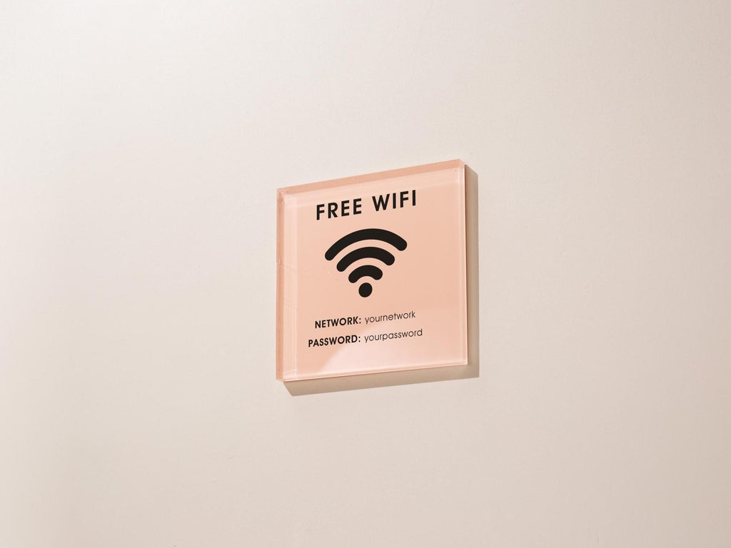 May include: A square, pink acrylic sign with black text and a wifi symbol. The sign reads 'FREE WIFI' at the top, with a wifi symbol in the center. Below the symbol, it lists 'NETWORK: youmetnetwork' and 'PASSWORD: yourpassword'.